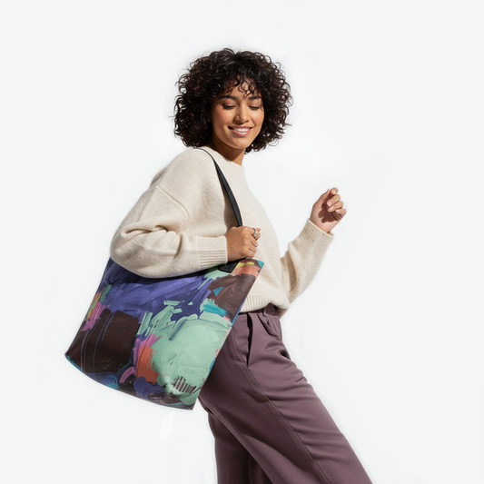 Woman carrying the Dragonfly Brush tote bag with sage green, indigo, and coral brushstrokes on an artistic canvas by TASHAU.